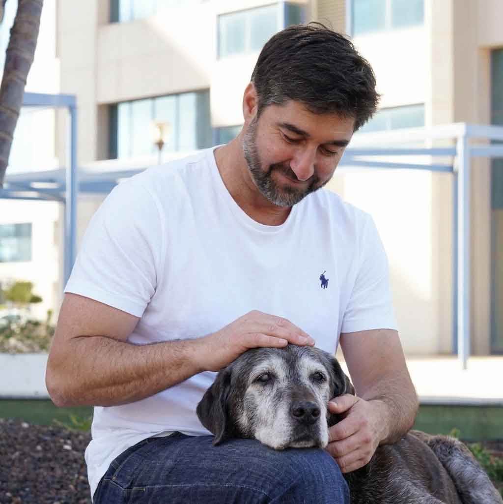 Andrés, especialista en bienestar canino senior, acariciando a un perro mayor con canas.